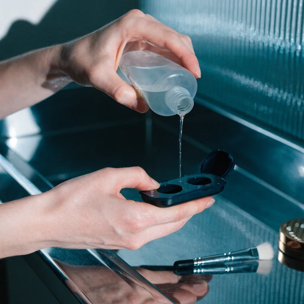 Clear solution bottle tipped mid-pour with a thin stream of liquid falling