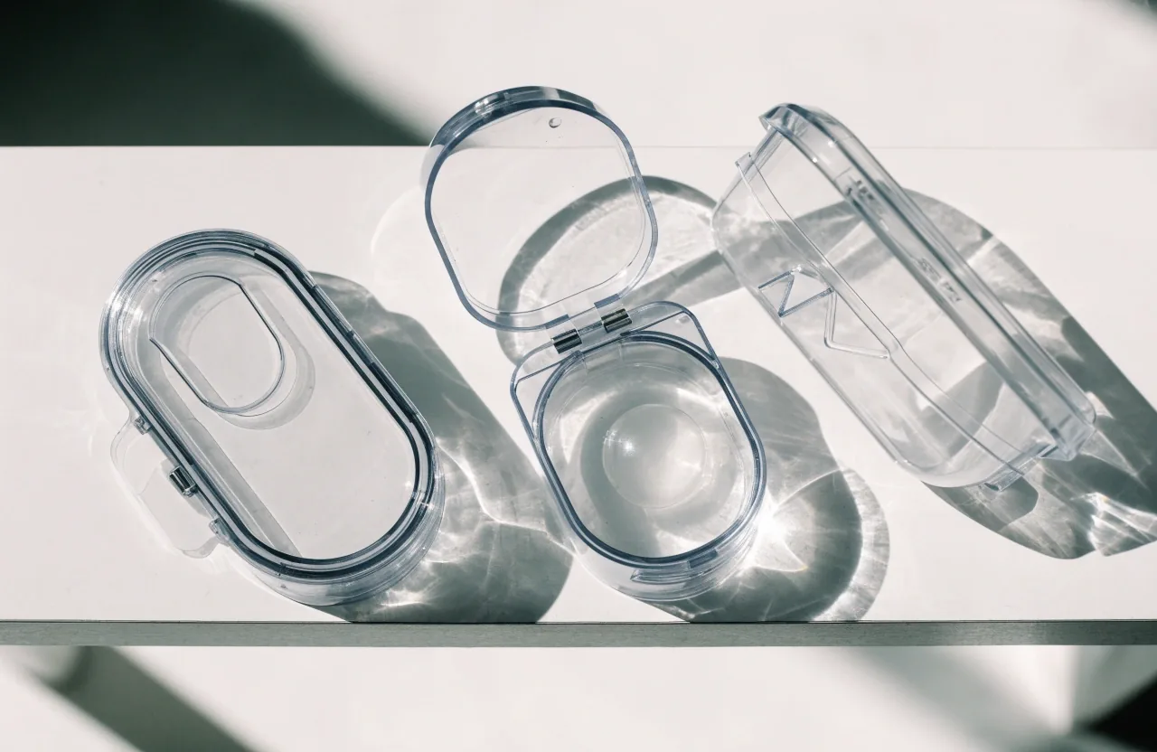 Three contact lens cases on a white bench: one closed, one open with a lens in solution, one empty